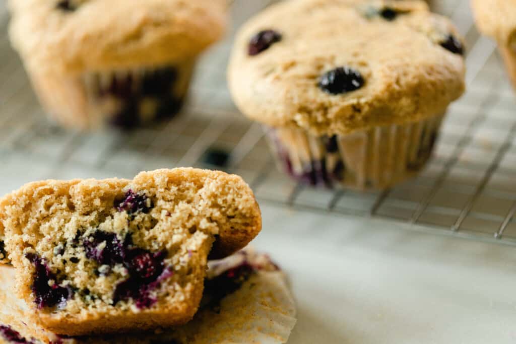 close up of a half of sourdough blueberry muffin on a countertop with more muffins on a wire rack in the background