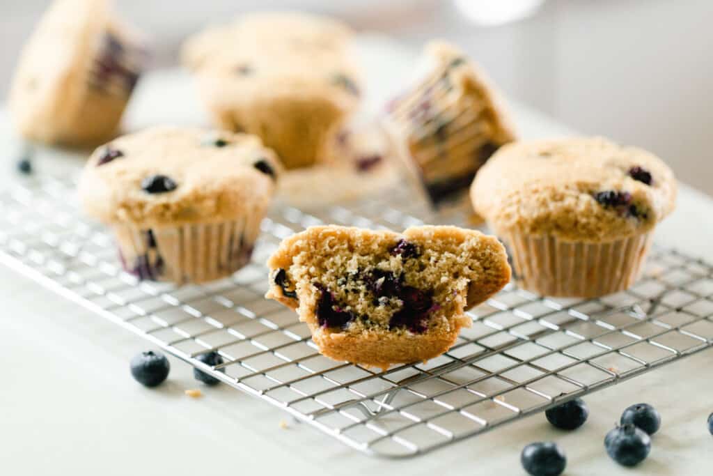 sourdough blueberry muffins on a wire rack on a white countertop with blueberries surrounding the rack