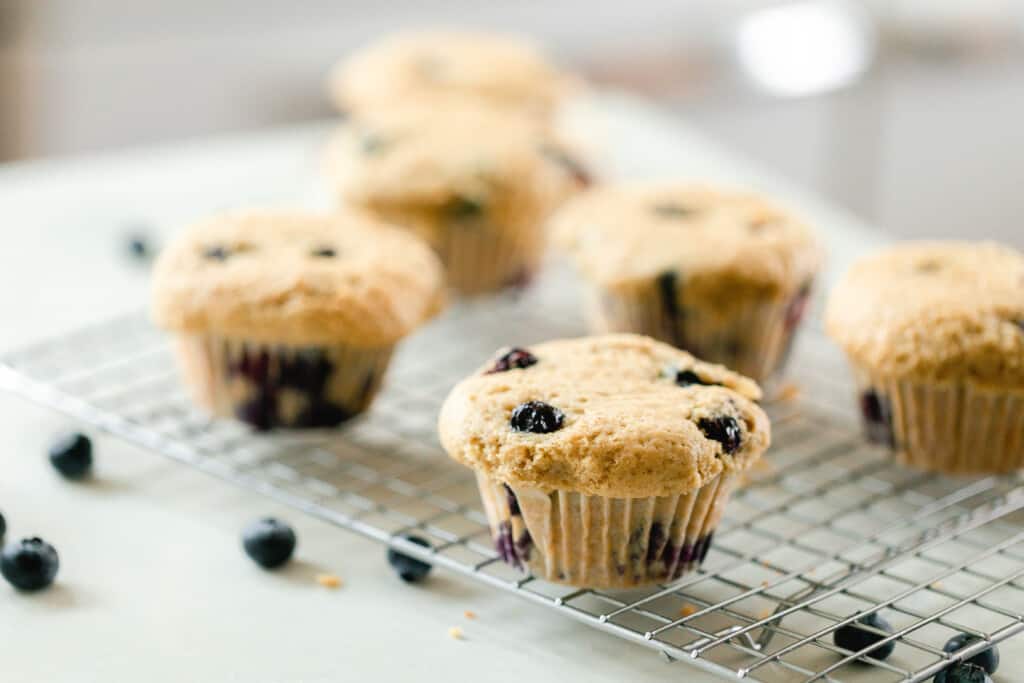 six sourdough blueberry muffins on a wire rack on a white quartz countertop with fresh blueberries sprinkled around