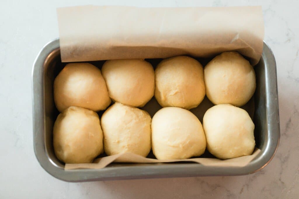 sourdough brioche dough rolled into balls and placed in a parchment lined stainless loaf pan