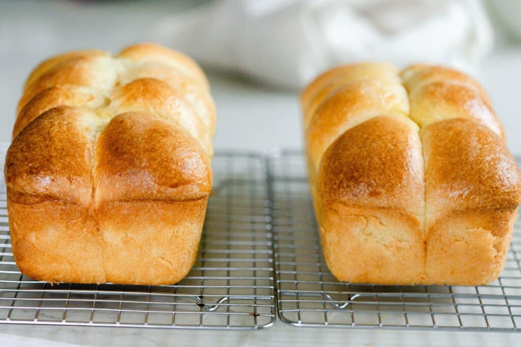 the front of two loaves of sourdough brioche on a wire rack on a white countertop with a white towel in the background