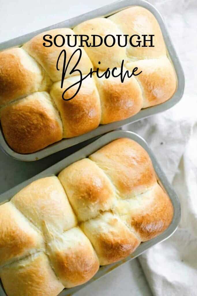 overhead photo of two loaves of sourdough brioche in stainless loaf pans on a white countertop and white towel