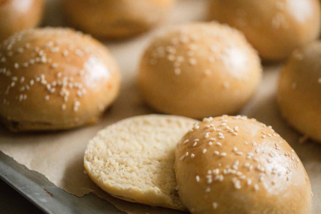 up close picture sourdough hamburger buns on a parchment lined baking sheet