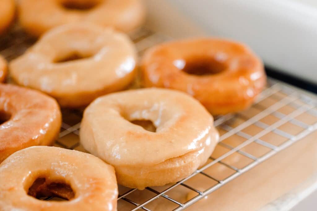 close up picture of fluffy glazed sourdough donuts drying on a wire rack with parchment underneath