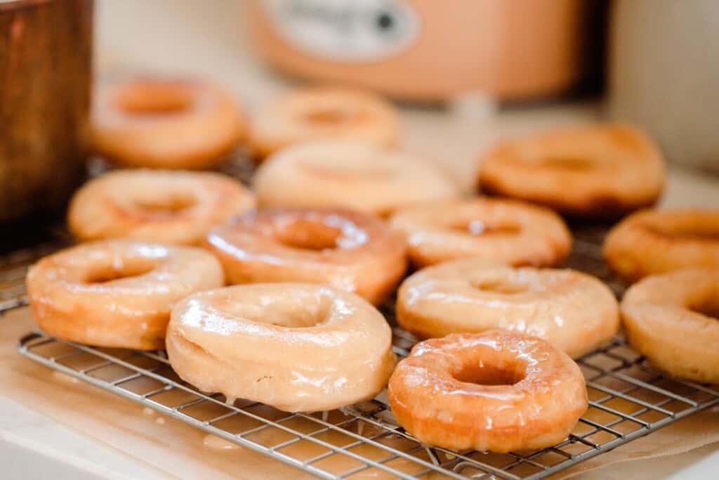 fluffy sourdough donuts with a vanilla glaze drying on a wire rack over parchment paper on a quartz countertop