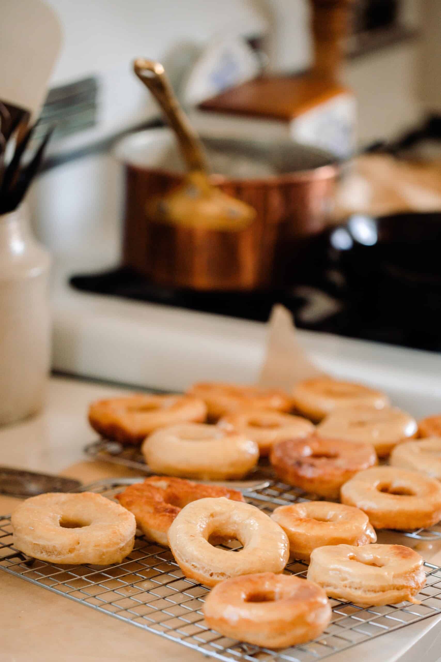 glazed sourdough donuts stacked on a wire rack next to a white vintage stove with a copper pot on the stove