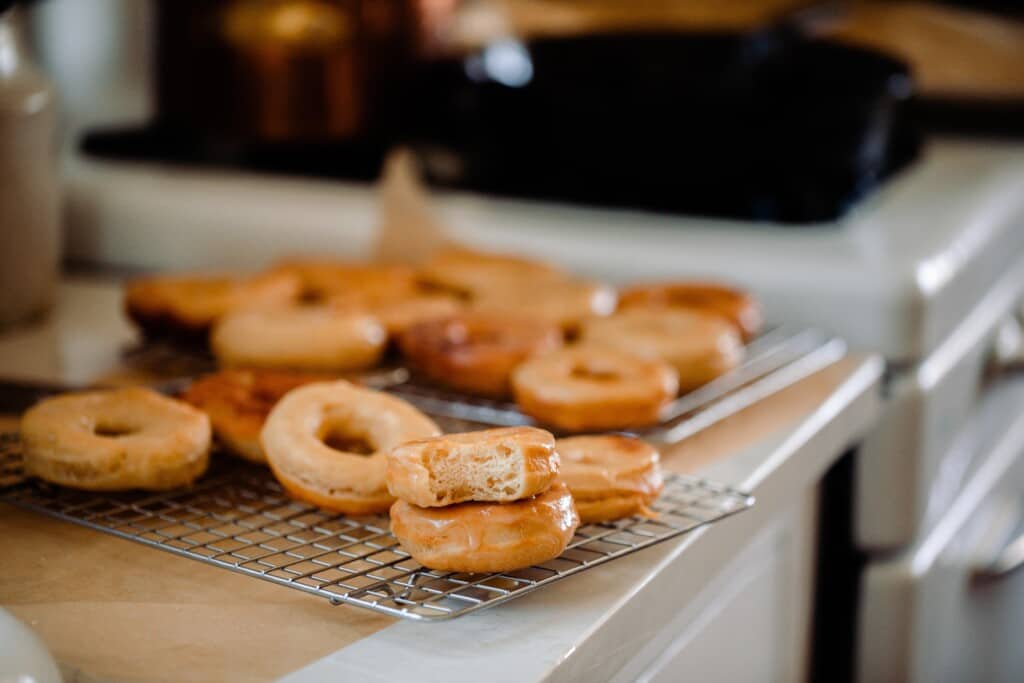 sourdough donuts piled on a wire rack over parchment paper on a white quartz countertop. There are two donuts stacked on top of each other with a. bit taken out of the top donut