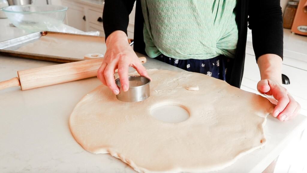 woman wearing a baby is cutting out rolled donut dough on a white countertop