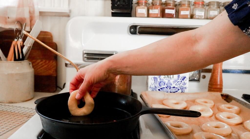 adding donuts to a hot cast iron skillet with coconut oil