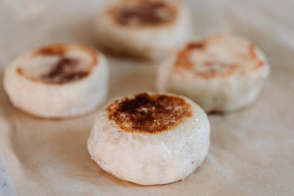 four sourdough English muffins placed on parchment paper.