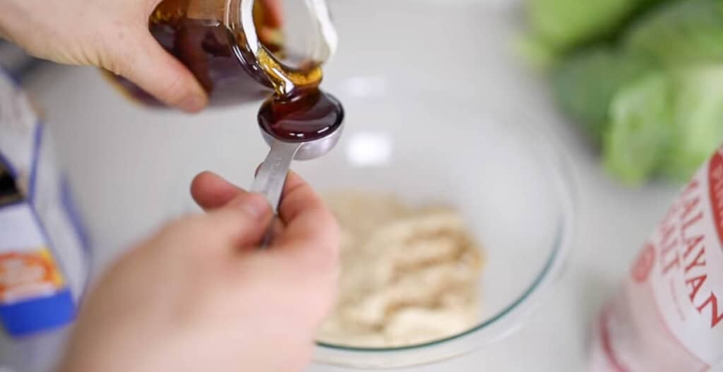 adding honey to dough in a glass bowl on a white countertop