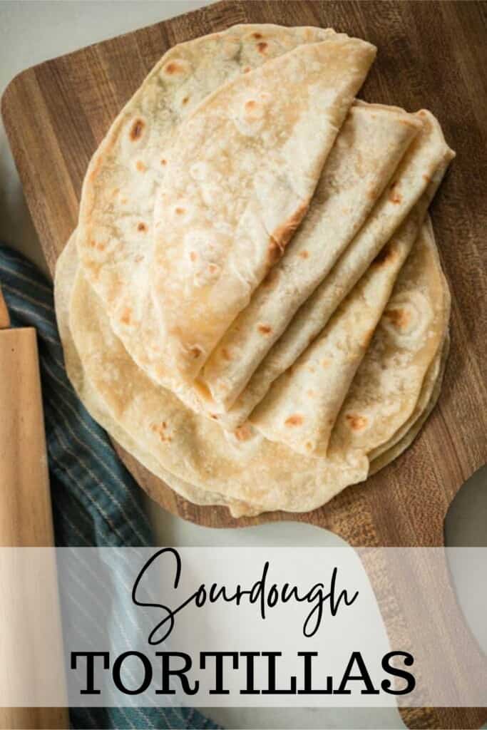 overhead photo of sourdough tortillas folded in half on a wood cutting board with a blue towel with a rolling pin to the back left