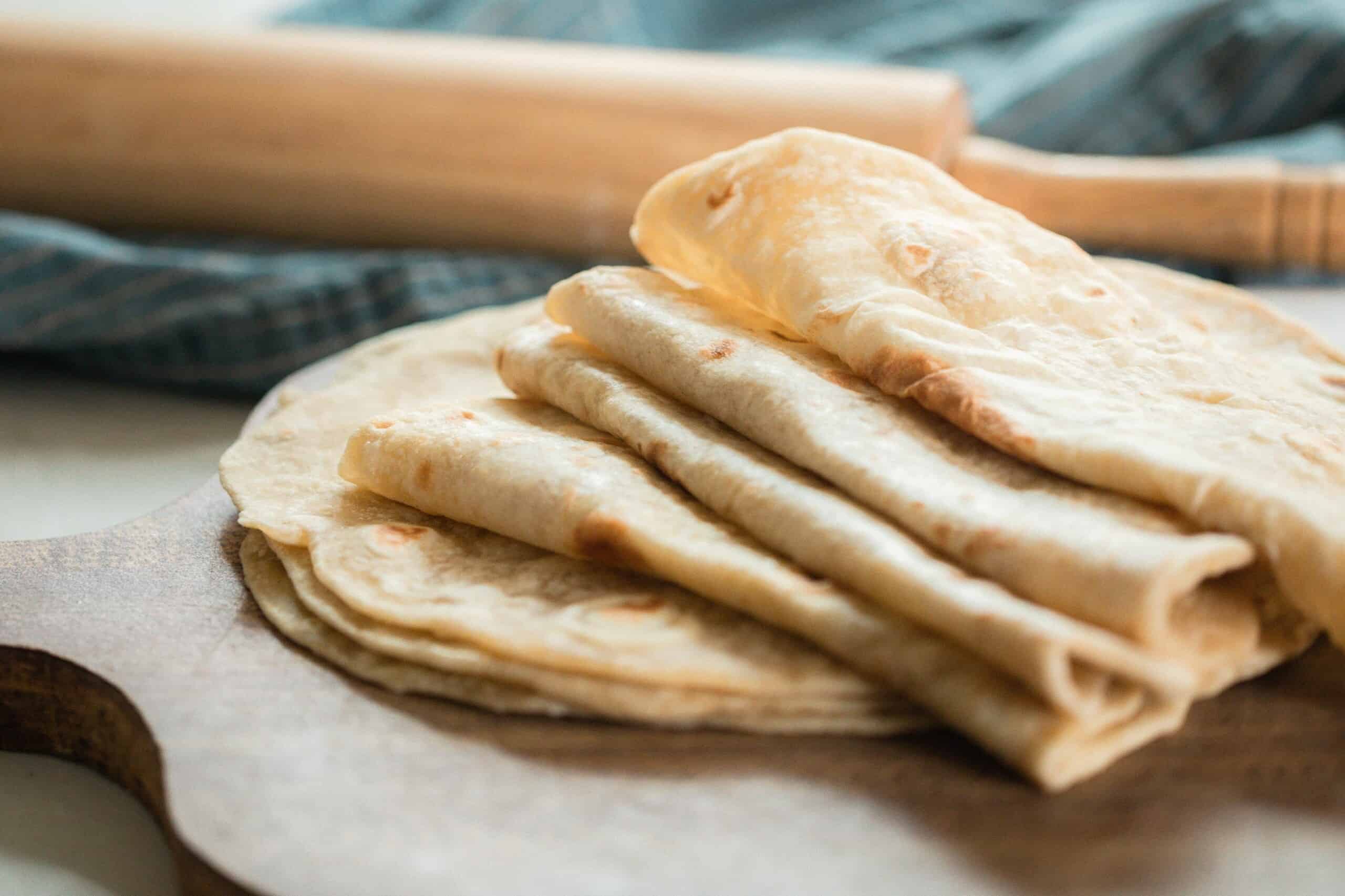 sourdough tortillas folded in half on a white quarts countertop with a blue towel with a rolling pin resting on top in the background