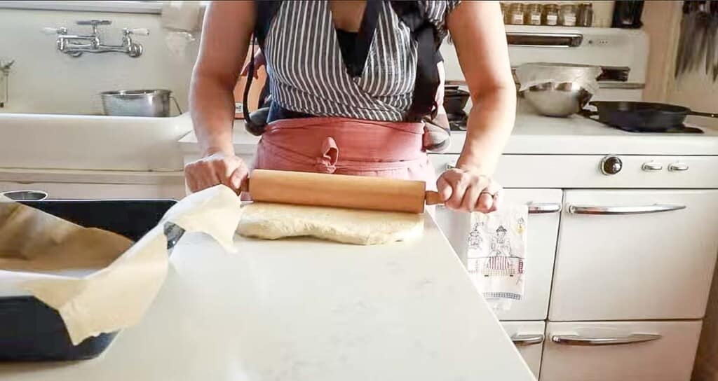 woman rolling out dough on a white quartz countertop with a wooden rolling pin