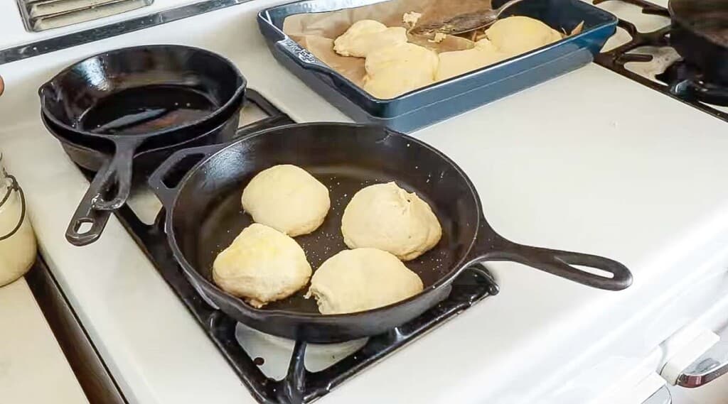 Sourdough English muffins cooking in a cast iron on a white vintage stove