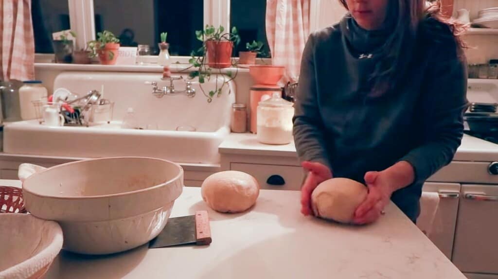 woman shaping sourdough bread with hands on a white countertop