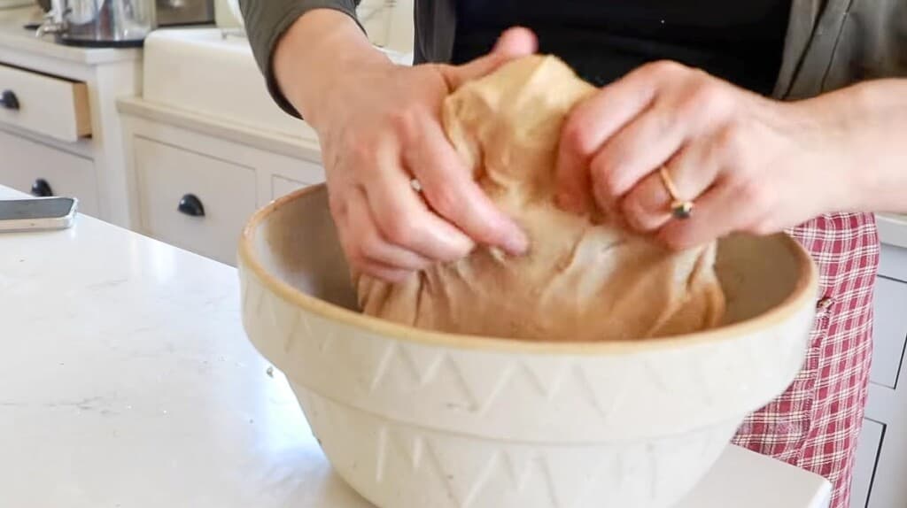 hands pulling dough on our a bowl to do a stretch and fold method of kneading dough