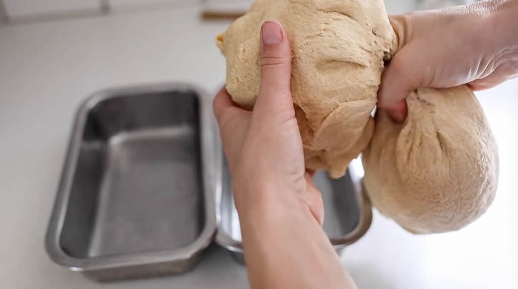 splitting whole wheat sourdough bread dough into two loaves with stainless loaf pans right behind the dough