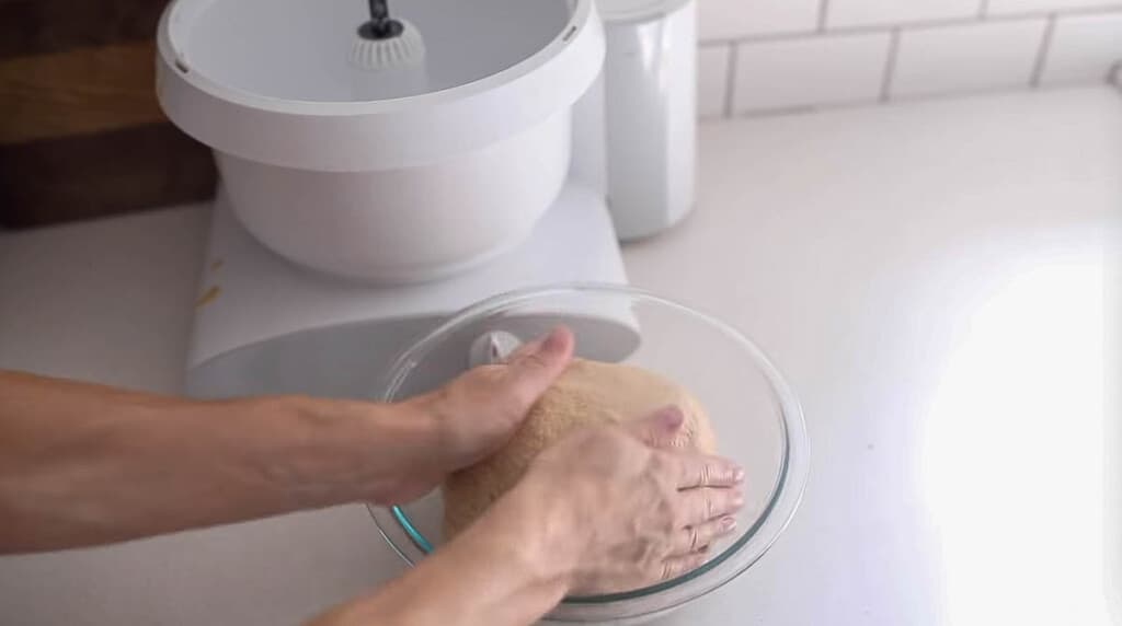 hands shaping dough in a glass dish on a white countertop