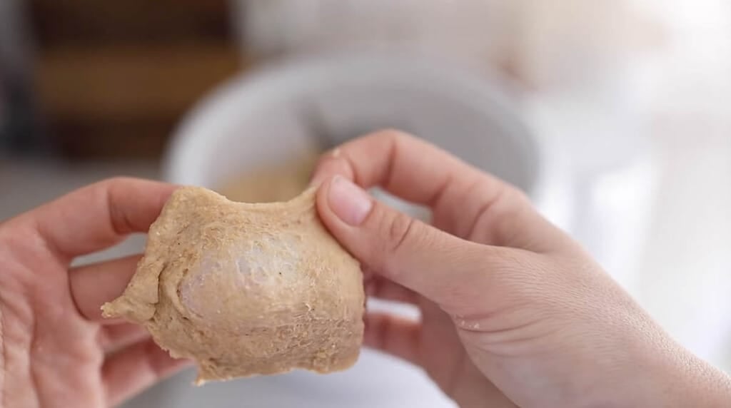 hands holding and stretching sourdough bread dough with a mixer in the background