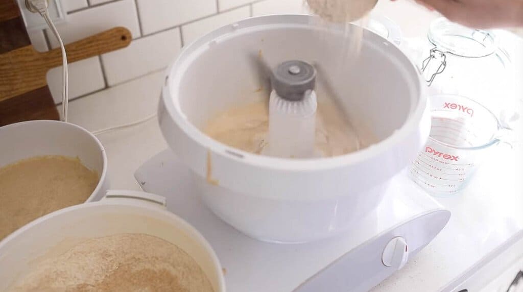 adding flour to a Bosch mixer on a white countertop