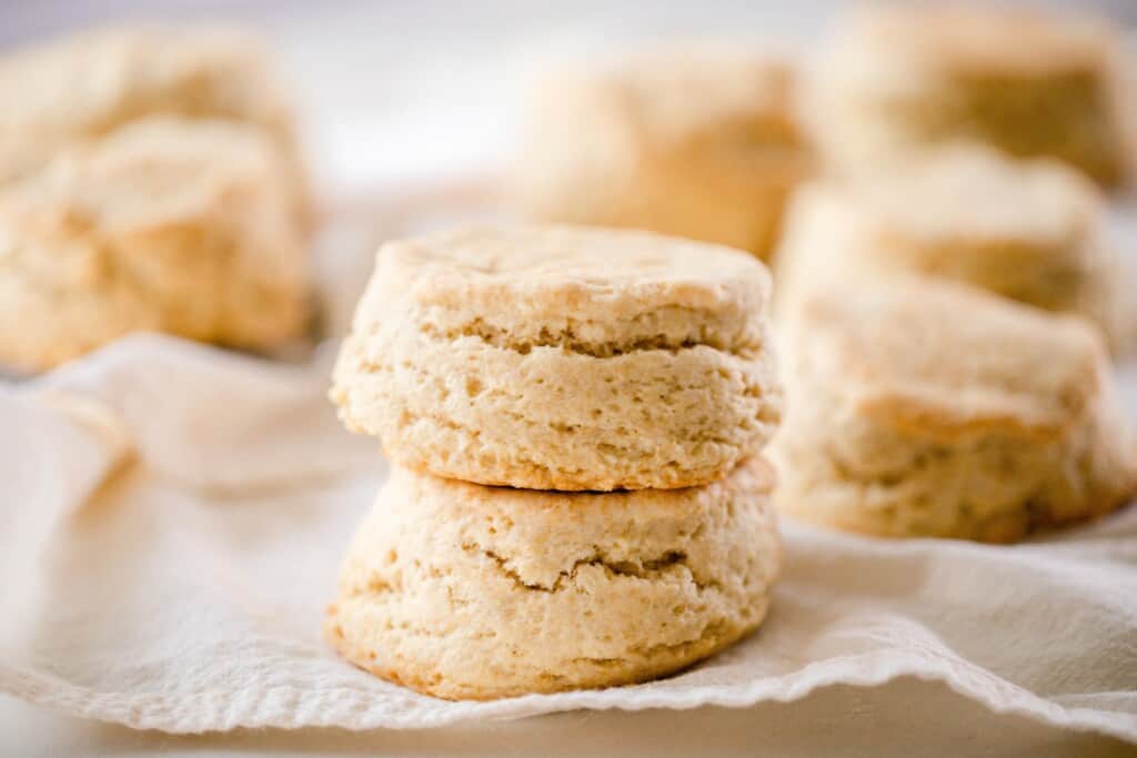 two fluffy sourdough biscuits stacked on top each other on a linen towel with stacks of more biscuits in the background