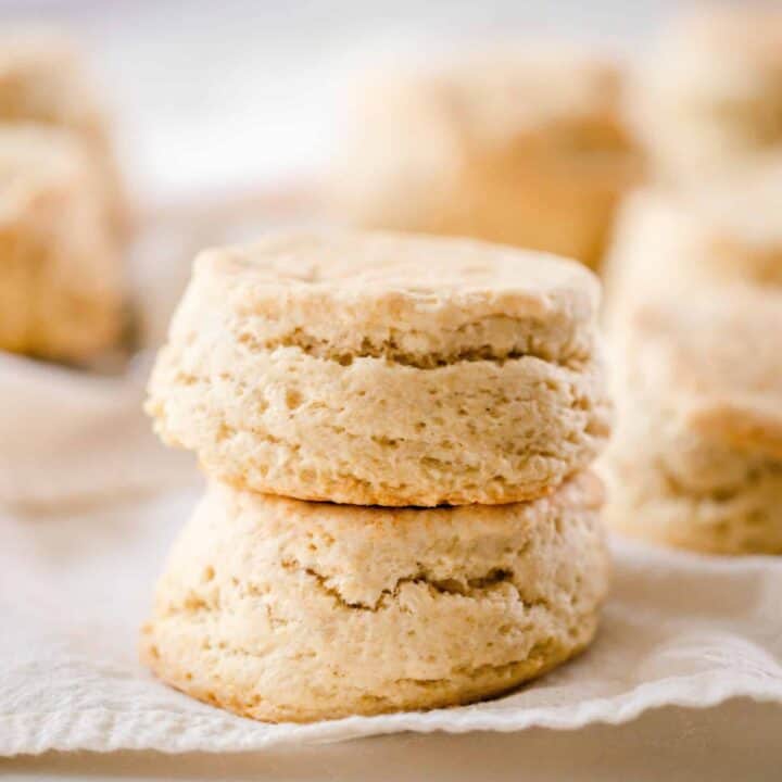 two fluffy sourdough biscuits stacked on top each other on a linen towel with stacks of more biscuits in the background