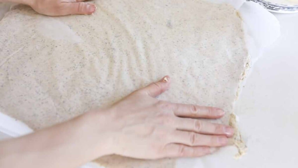 hands spreading out cracker dough between two pieces of parchment paper