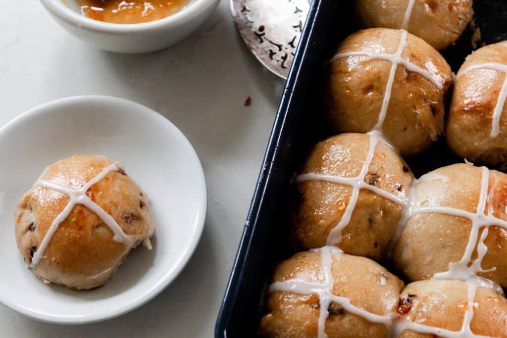 hot cross buns in a baking dish with a small white plate to the left with another bun