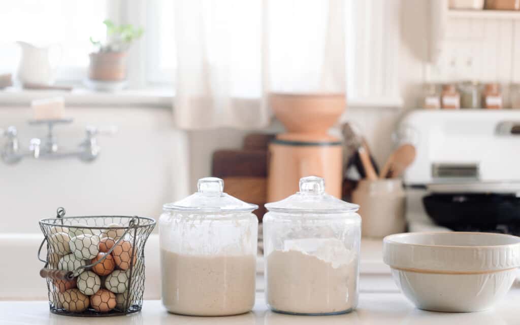 sourdough pasta ingredients: eggs, sourdough starter, and flour on a white quartz countertop next to a large stoneware bowl