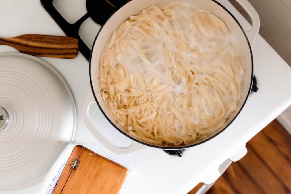 overhead photo of sourdough pasta cooking in boiling water in a white dutch oven