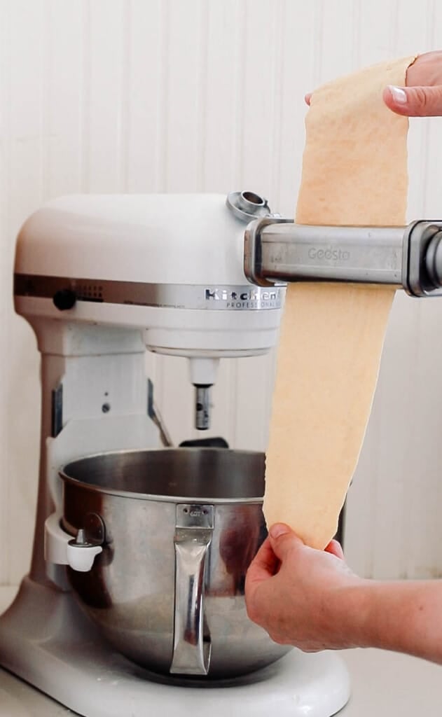 placing sourdough pasta dough through a pasta maker attachment for the kitchenaid stand mixer