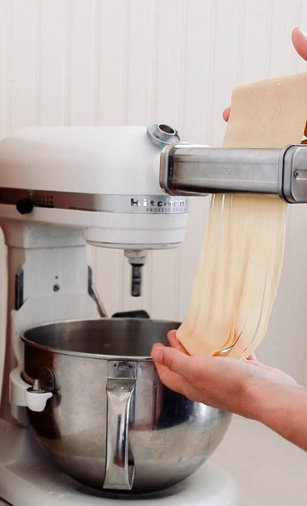 cutting pasta dough into fettuccine noodles in a pasta maker attachment on the Kitchenaid stand mixer.