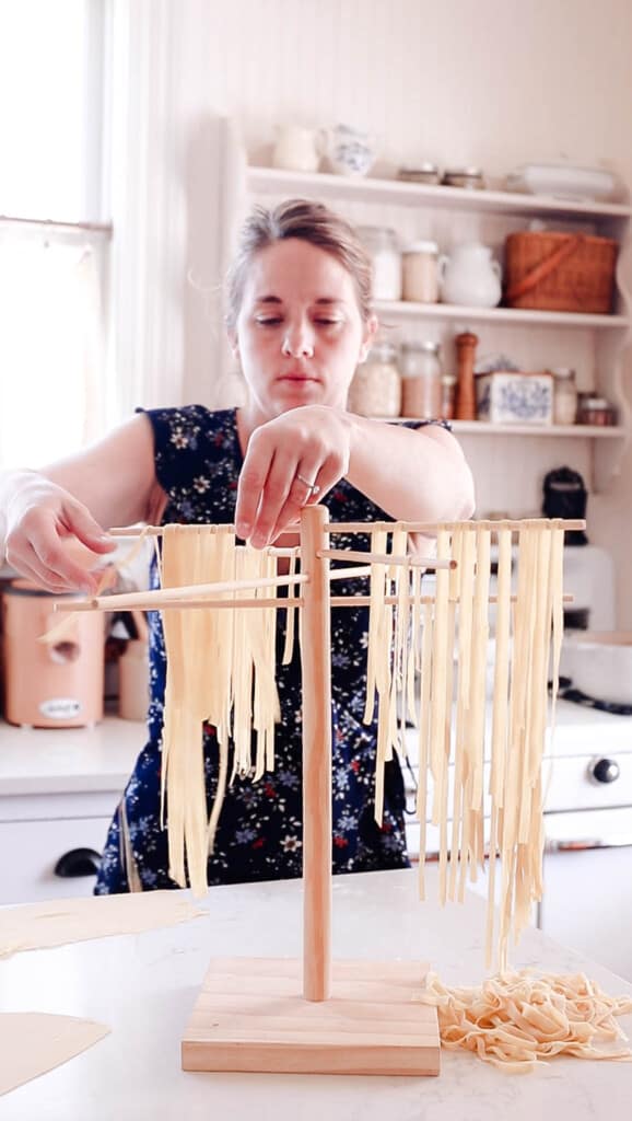 woman placing fresh sourdough noodles on a wooden pasta drying rack in her white kitchen