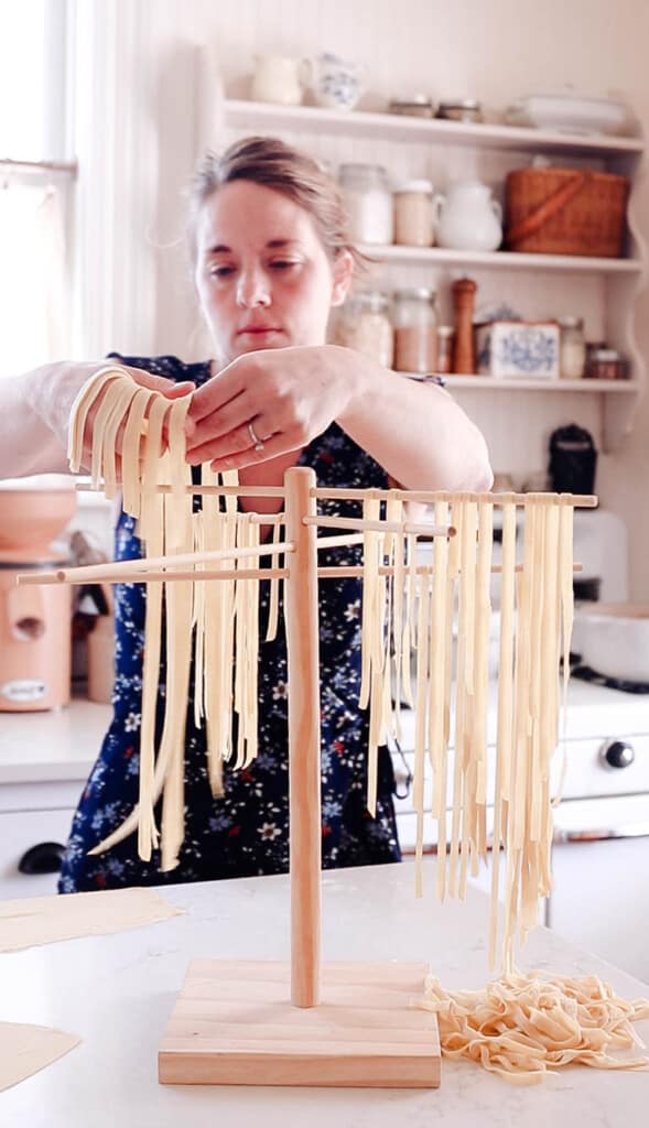 woman adding fresh sourdough pasta to a pasta drying rack in her white farmhouse kitchen