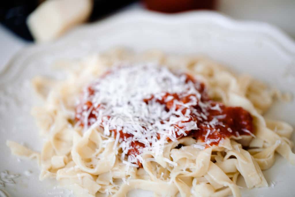 close up picture of homemade sourdough noodles topped with marinara sauce and fresh parmesan cheese on a white plate