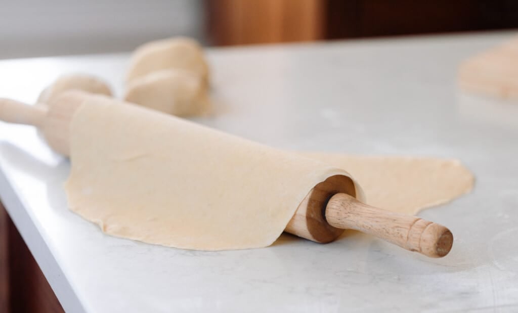 sourdough pasta dough rolled out flat and draped over a wooden rolling pin on a white countertop