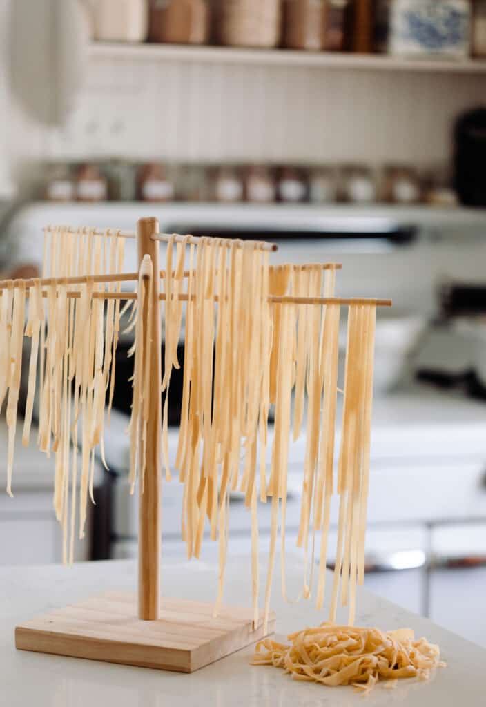 Fresh sourdough pasta hanging on a wooden pasta drying rack.