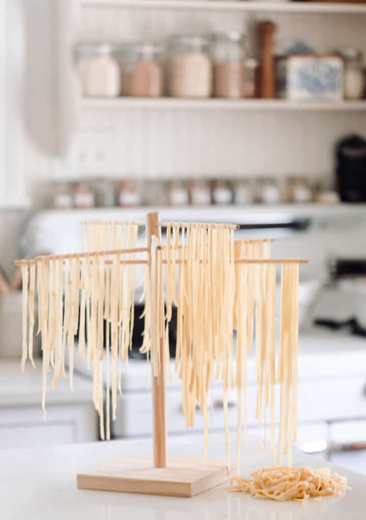 sourdough noodles drying on a pasta drying rack with a pile of noodles sitting to the right of the rack. An antique stove is in the background