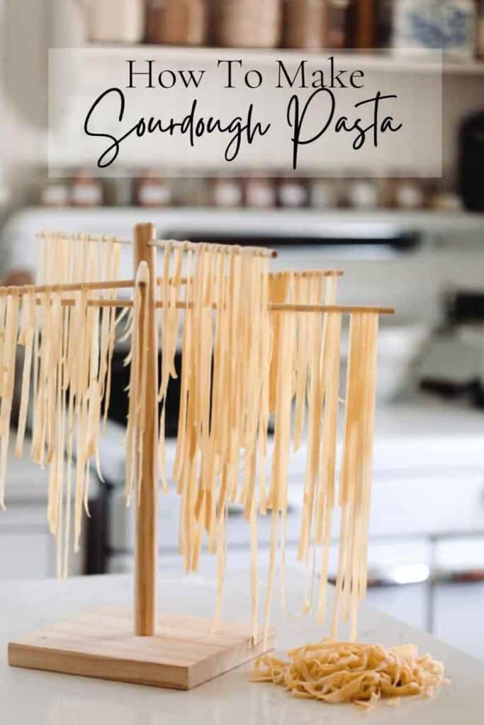 fresh sourdough pasta hanging on a wooden pasta drying rack with a pile of noodles resting on the counter to the right