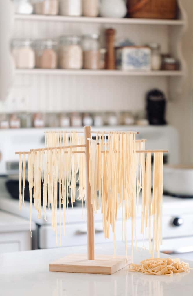 sourdough pasta hanging to dry on a wooden pasta drying rack in a white farmhouse kitchen