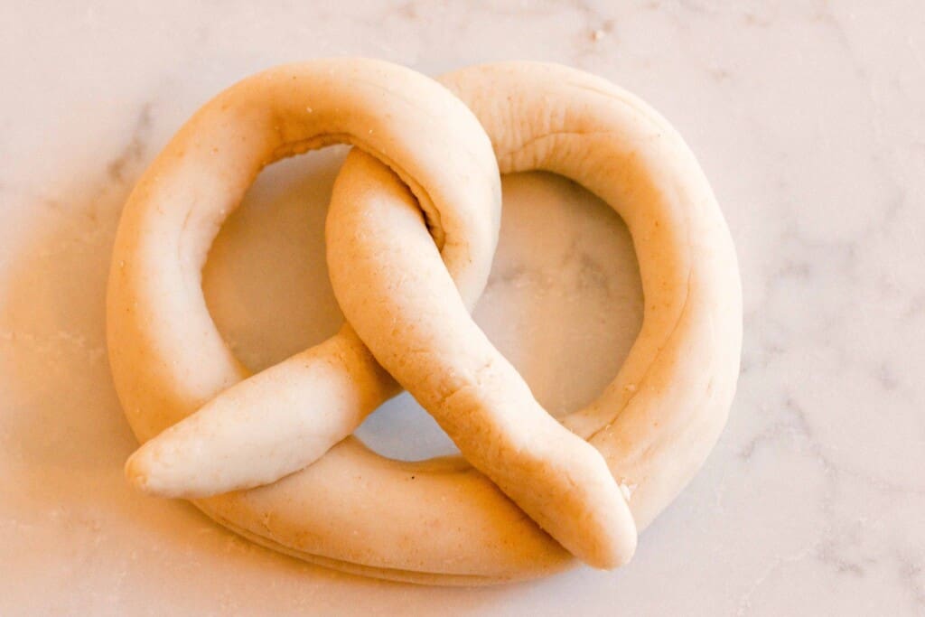 sourdough pretzel dough shaped into a pretzel shape on a white and gray quartz countertop