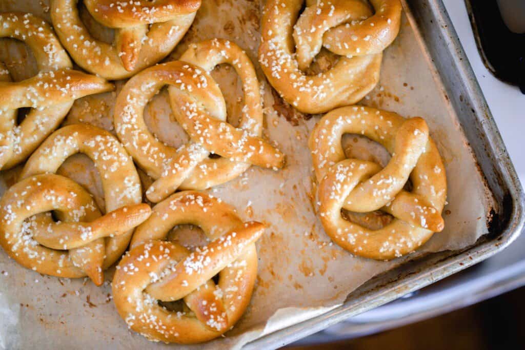 overhead photo of 7 homemade sourdough soft pretzels topped with course sea salt on a parchment lined baking sheet