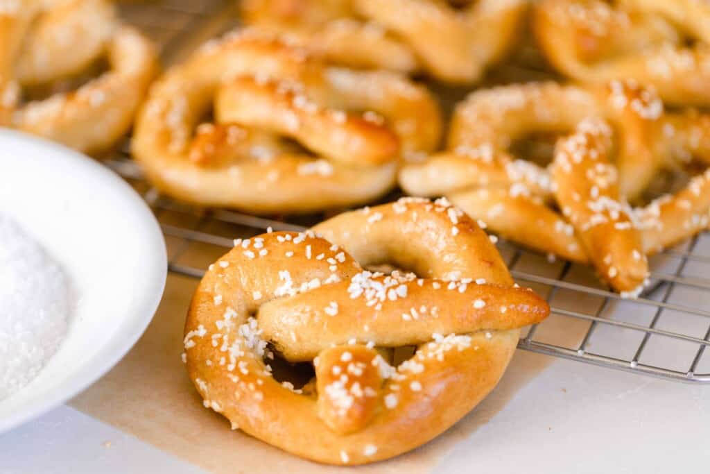 six sourdough pretzels layered on a counter and a wire cooling rack with a white bowl to the left