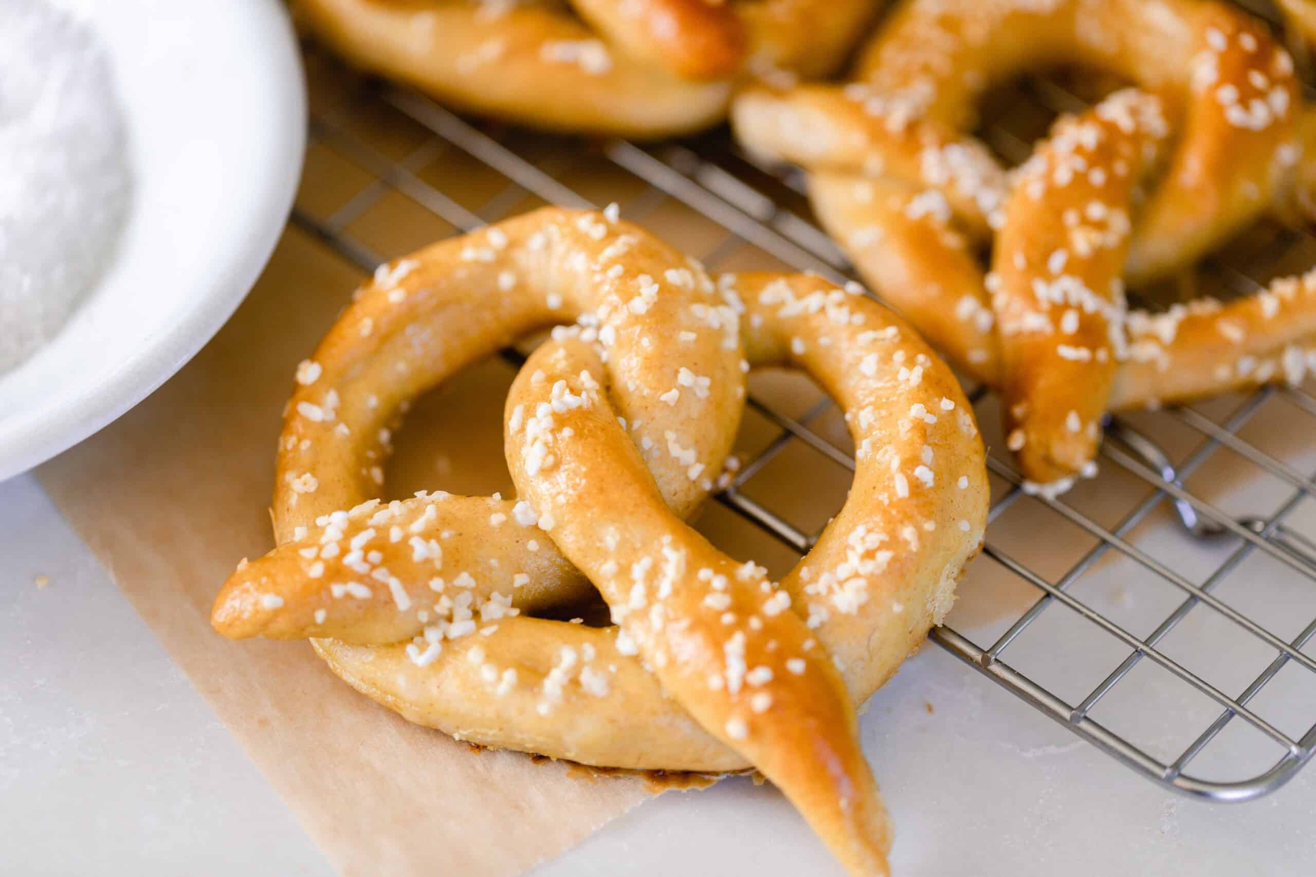 sourdough pretzel topped with course salt on a wire cooling wrack with more pretzels