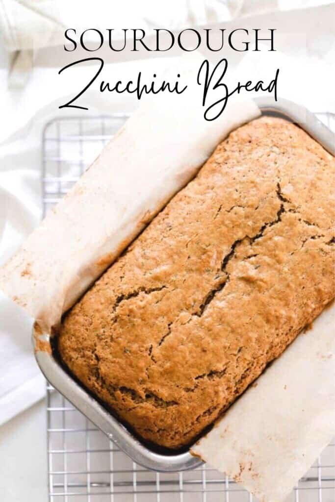 overhead photo of sourdough zucchini bread in a parchment lined stainless steel loaf pan on a wire rack over a white towel