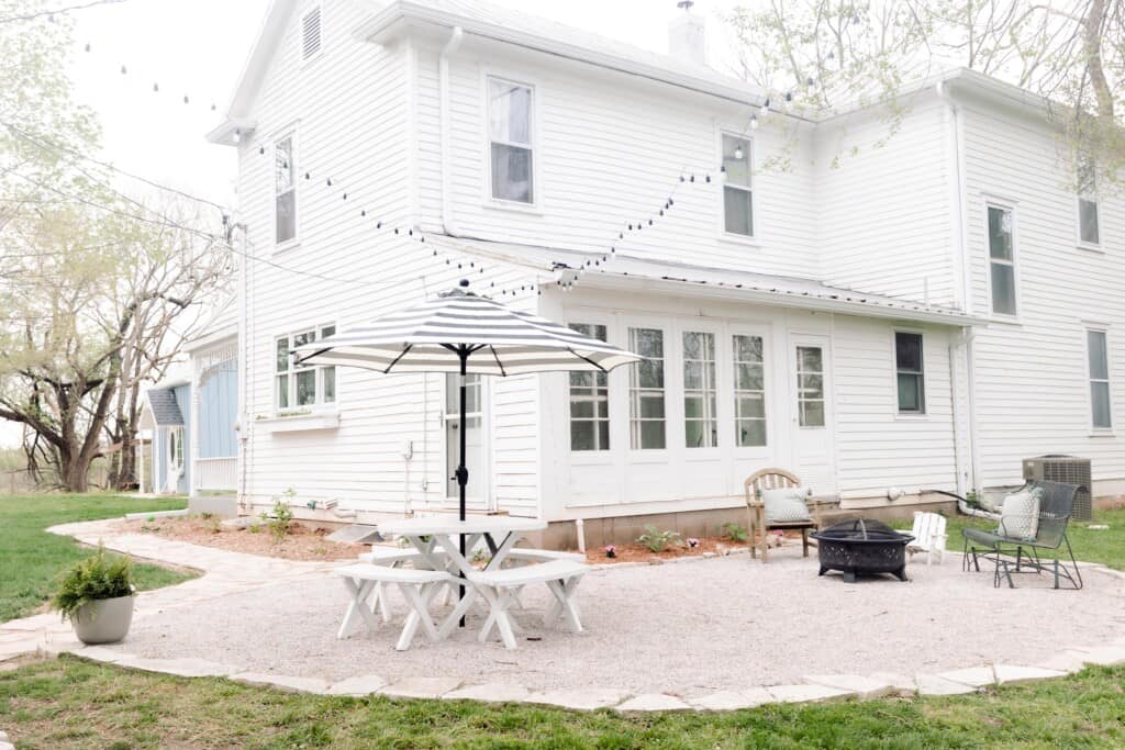 pea gravel patio with a flagstone boarder in the back of a white farmhouse