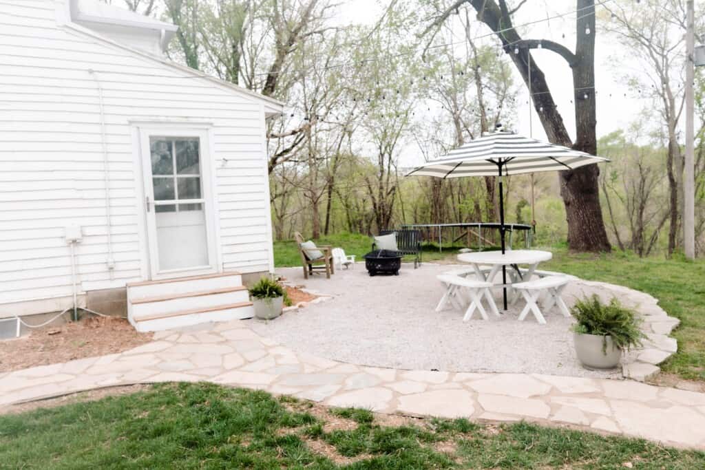 gravel patio lined with flagstone. The patio is off the side of a white farmhouse. 
