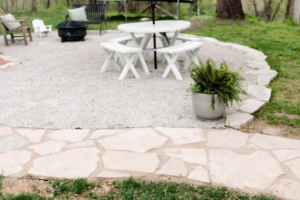 close up picture of a DIY pea gravel patio lined with flagstone with ferns and a table on the patio