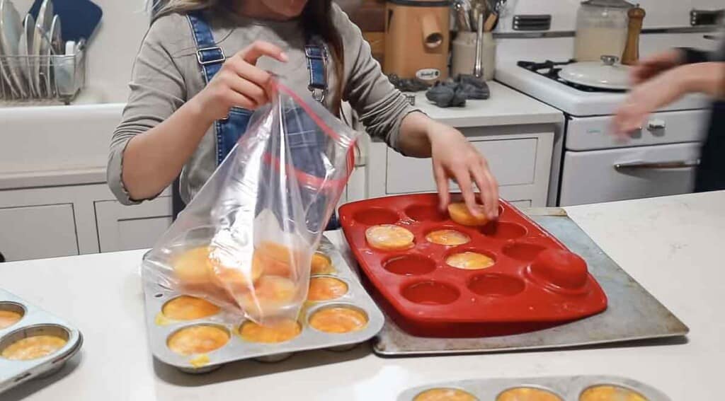 girl popping out frozen eggs from a red silicon muffin tin into a plastic bag